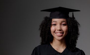 Portrait of a smiling graduate wearing a cap and gown, capturing a proud and joyful moment indoors.