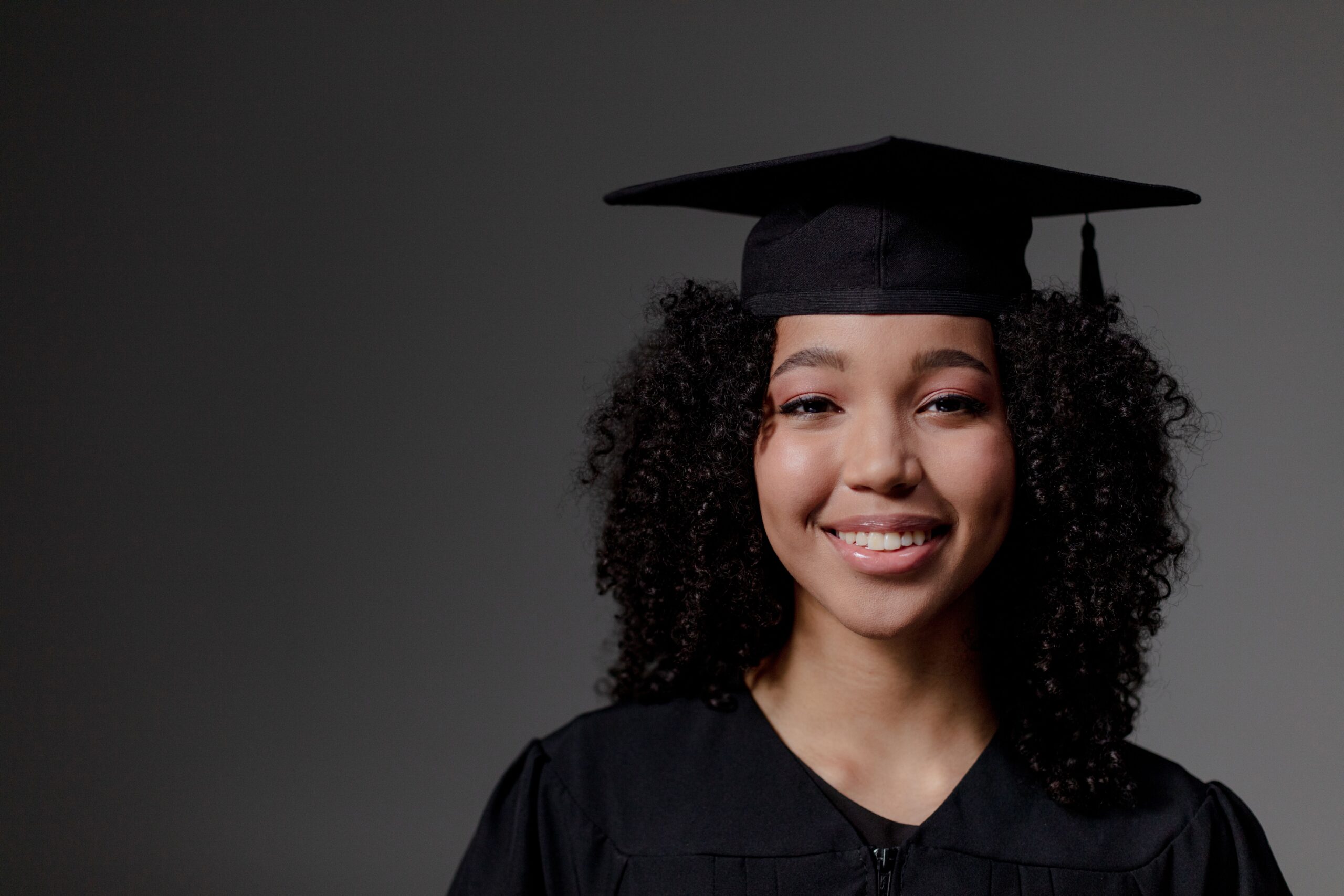 Portrait of a smiling graduate wearing a cap and gown, capturing a proud and joyful moment indoors.